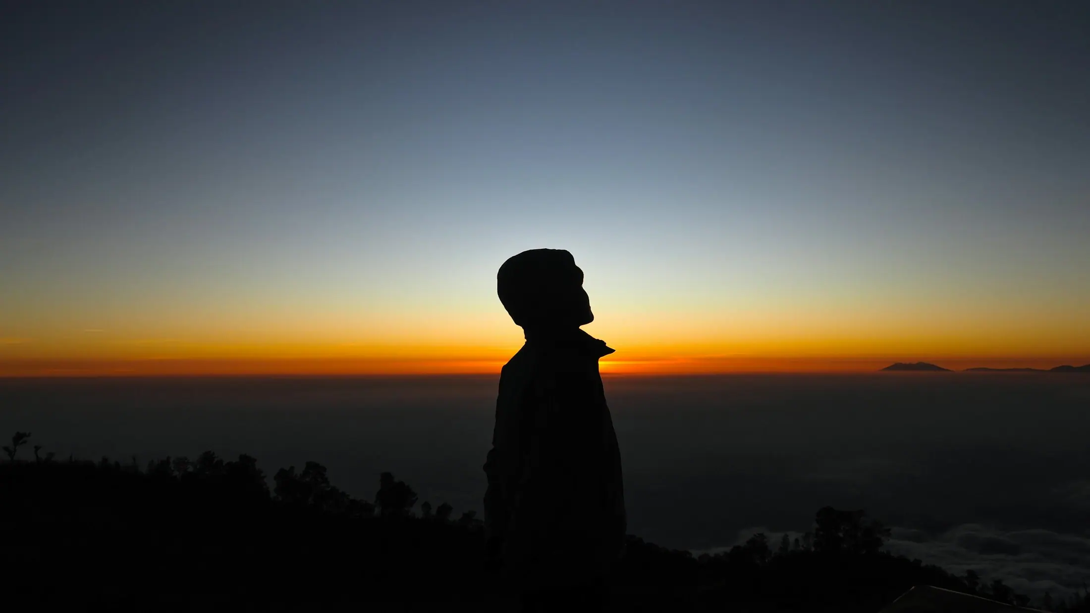 A figure in meditation silhouetted against a mountain sunrise